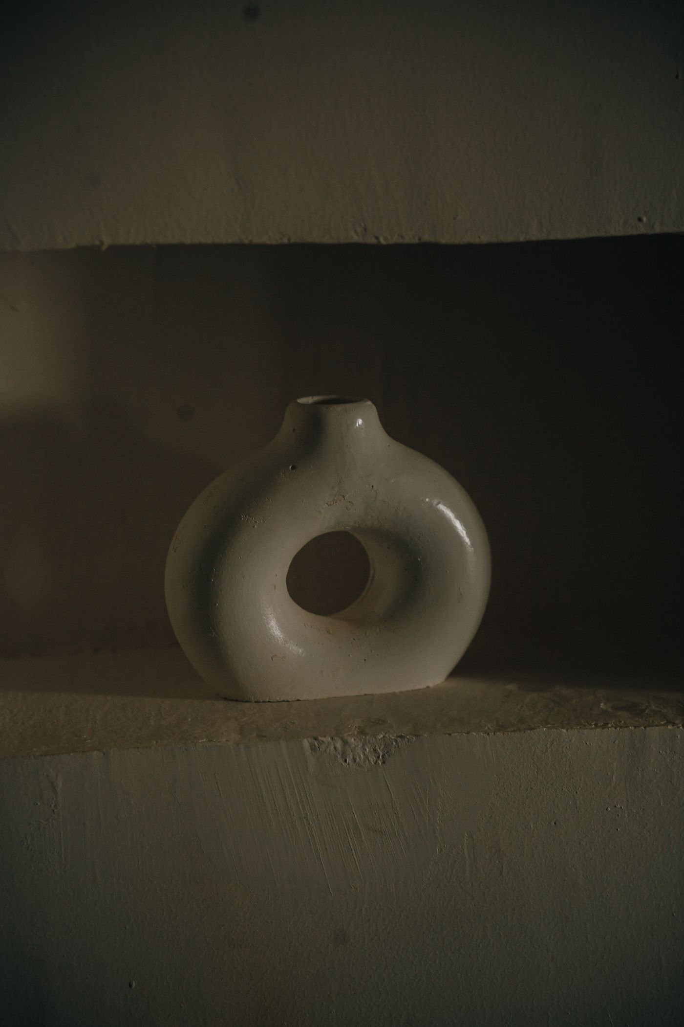A single pale ceramic form lit softly against a dark ground