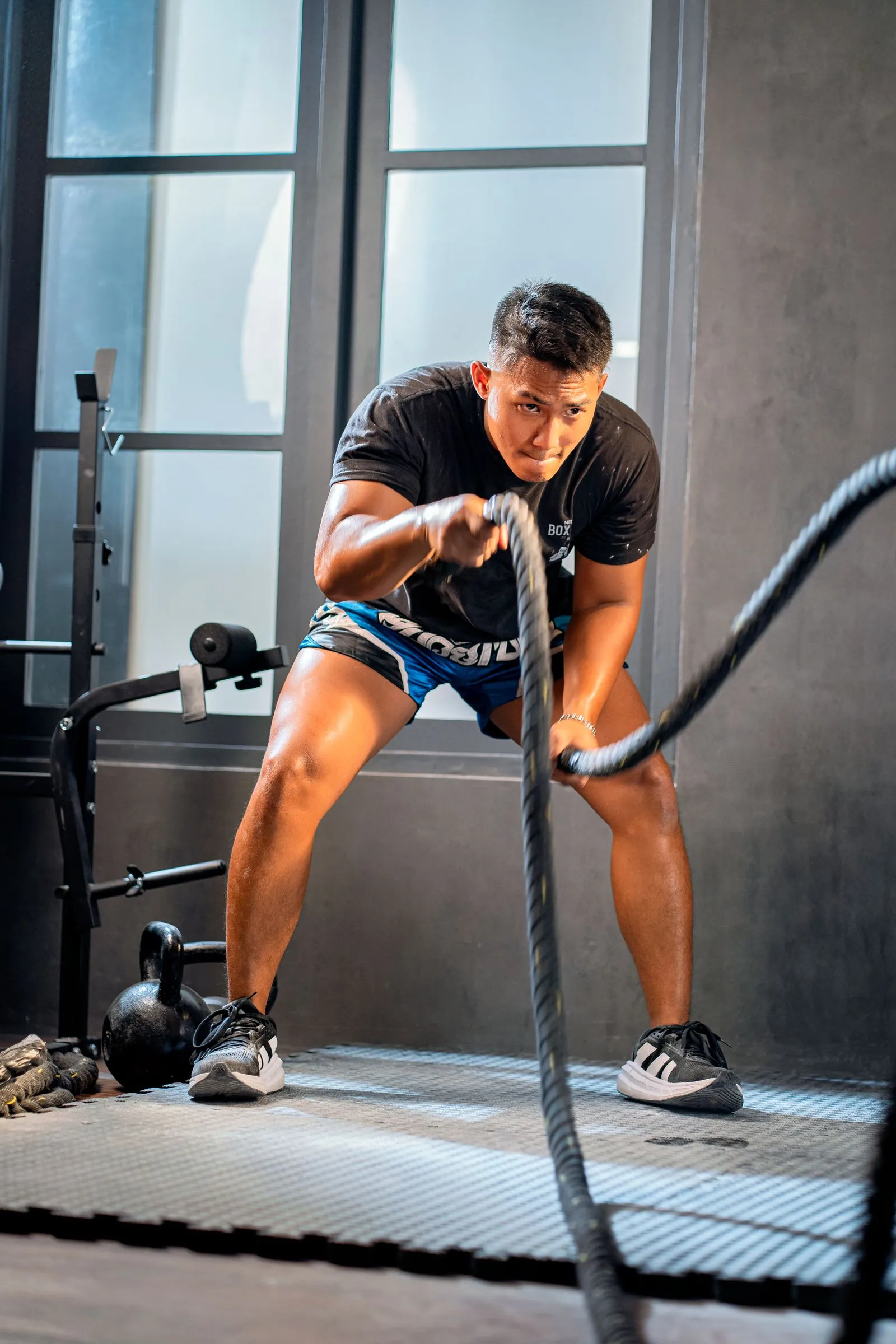 Athlete working battle ropes beside tall windows