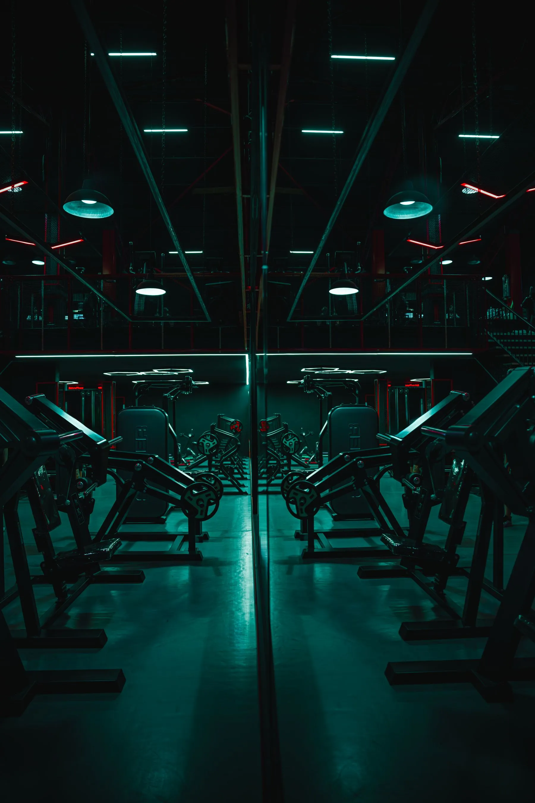 Darkened weight room with mirrored machines and teal light