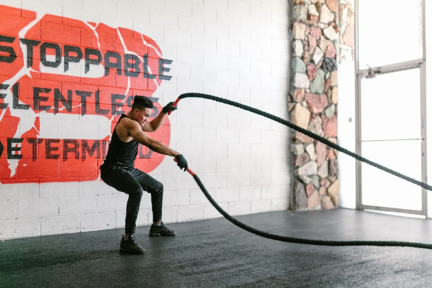 Athlete slamming battle ropes in front of a painted brick wall
