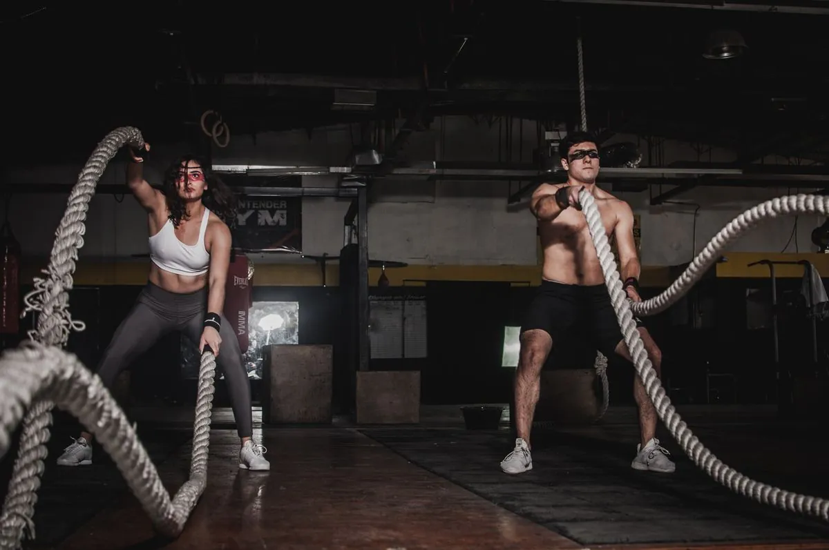 Two athletes working heavy battle ropes in a dark training hall