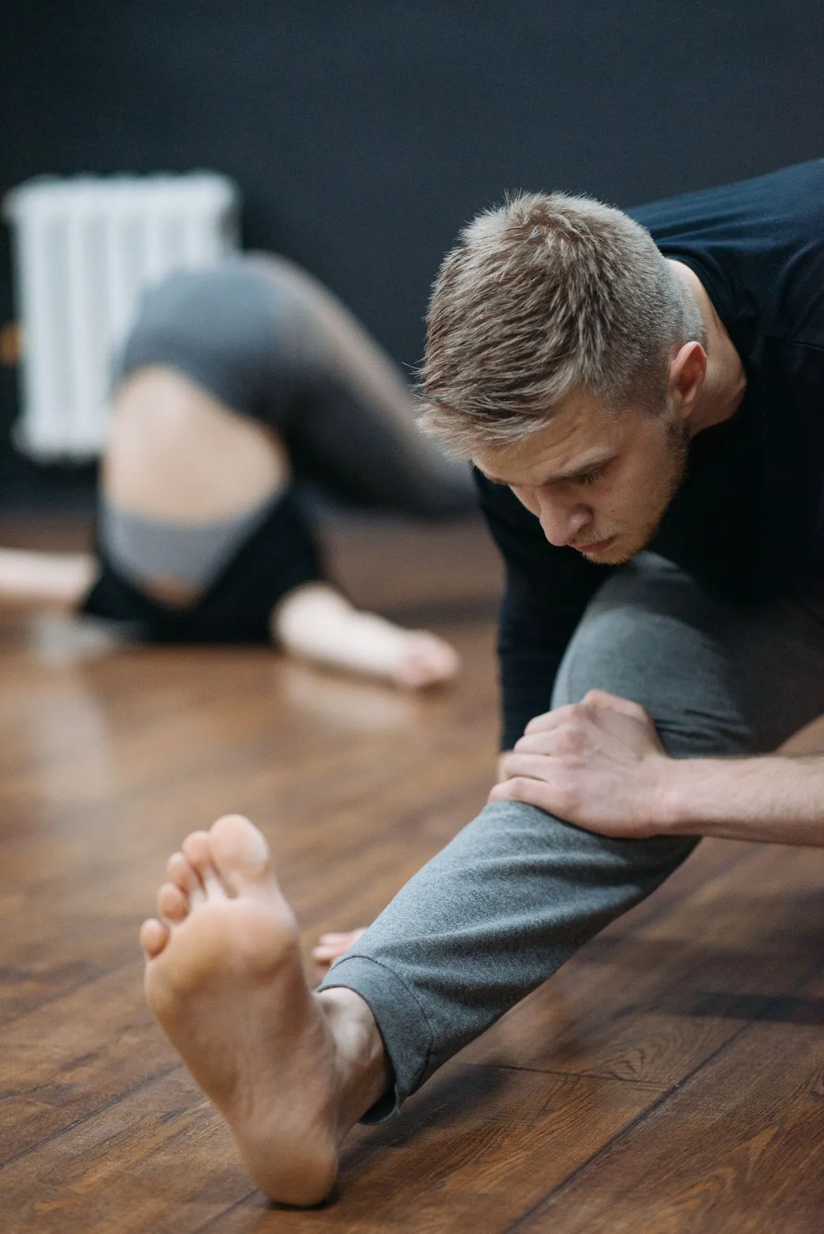 Barefoot athlete holding a deep seated stretch on a wood floor