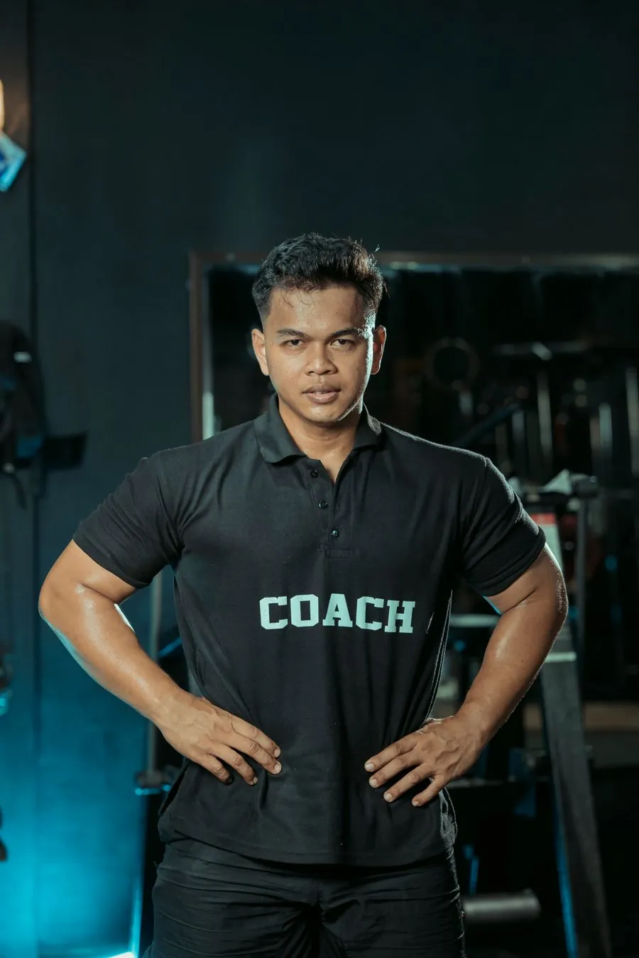 Coach in a black training shirt standing in a teal-lit gym