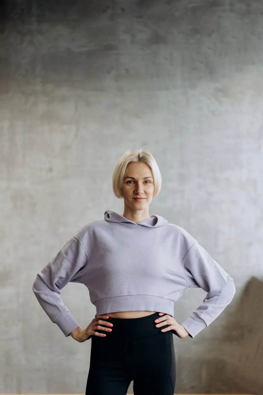 Person in a hoodie and leggings standing against a plain wall