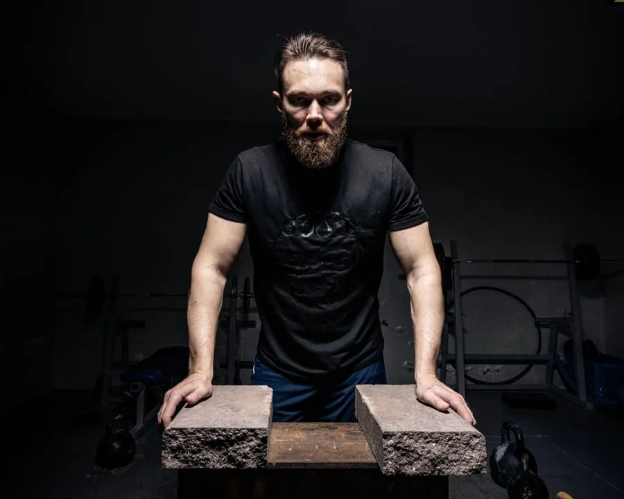 Person in a plain black t-shirt leaning on a bench in a dim gym