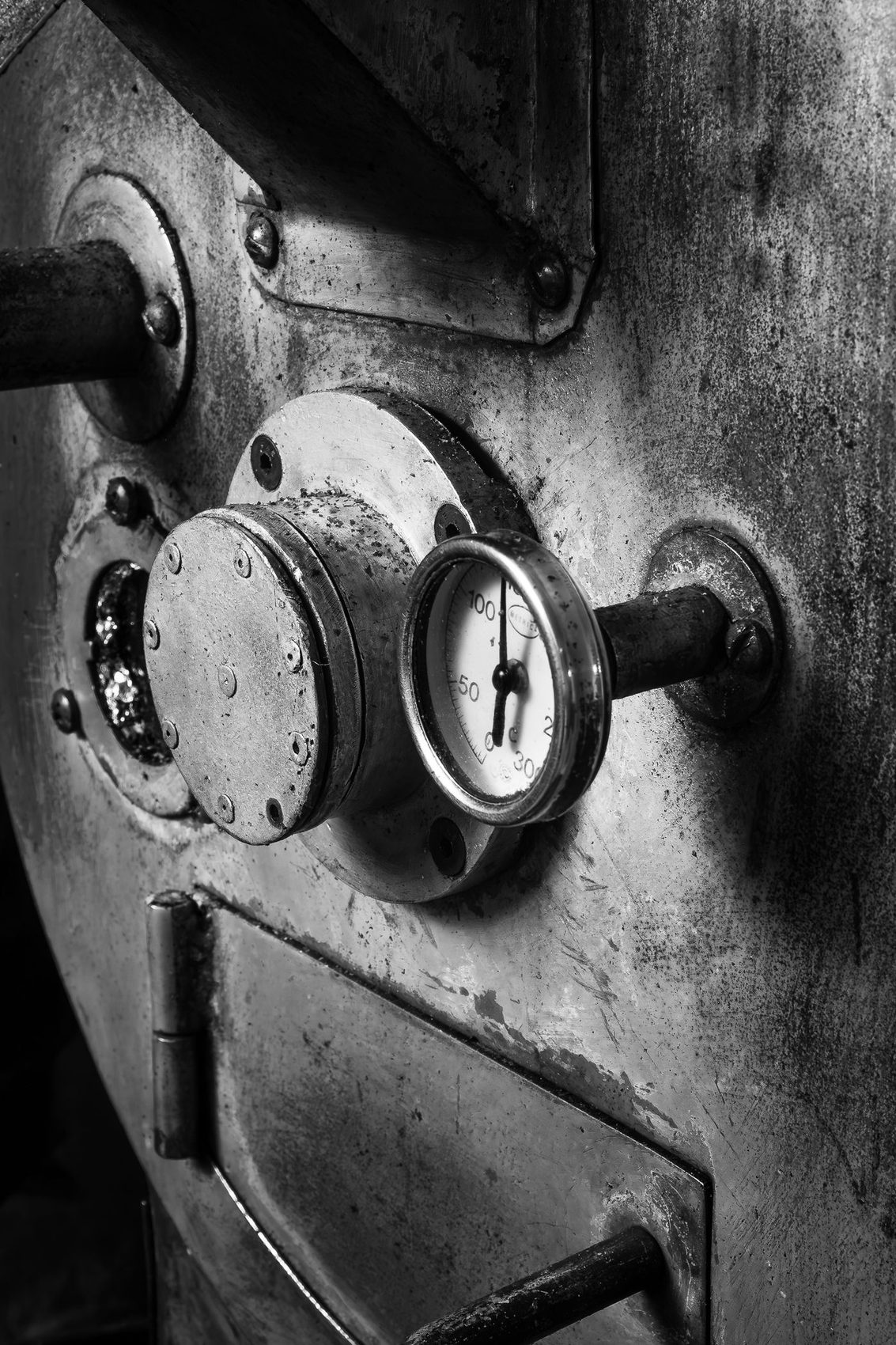 Monochrome close-up of a heavy roaster drum face and bolts