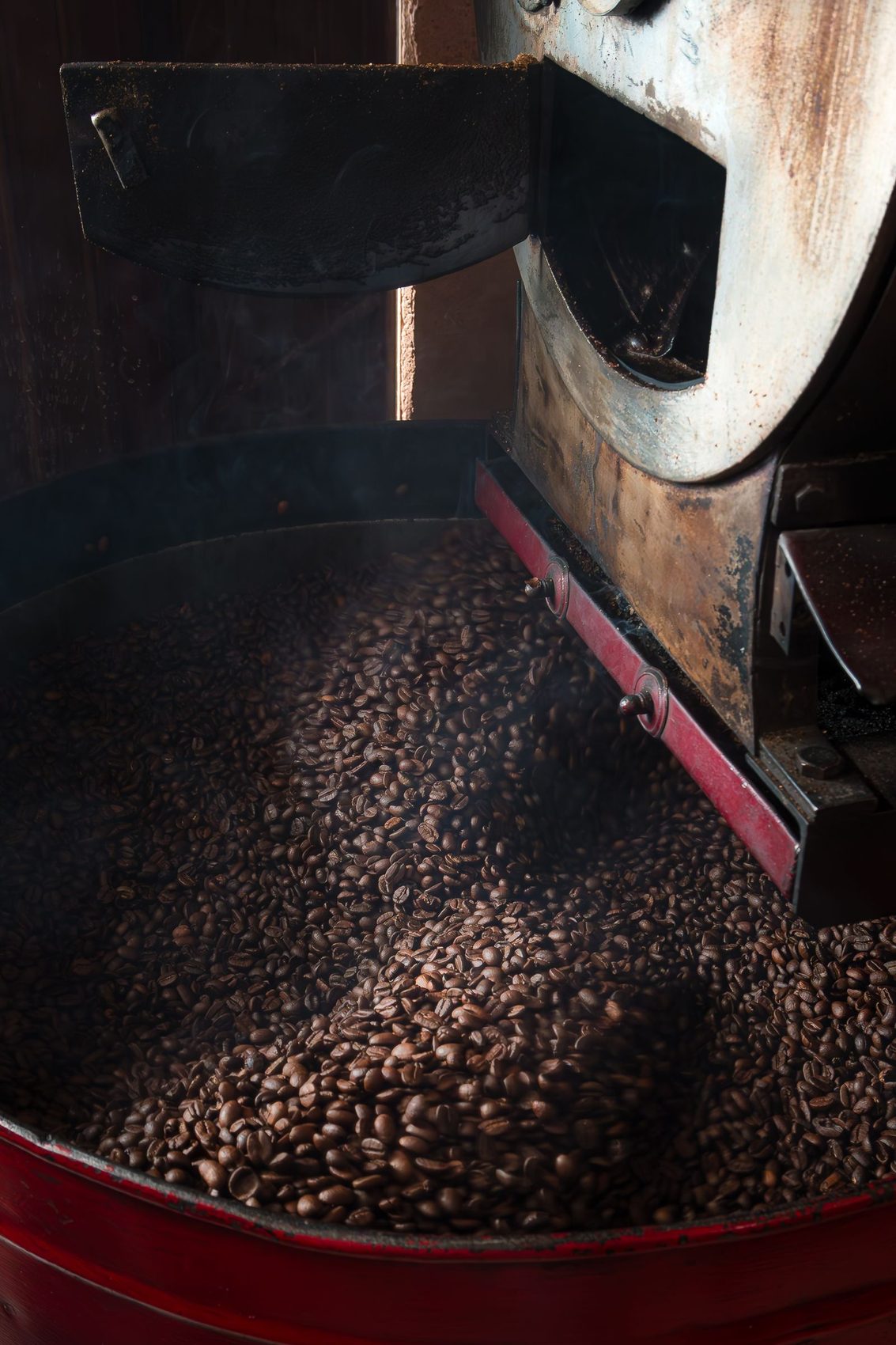 Warm-lit Kaldera industrial coffee roaster dropping roasted beans into the cooling bin