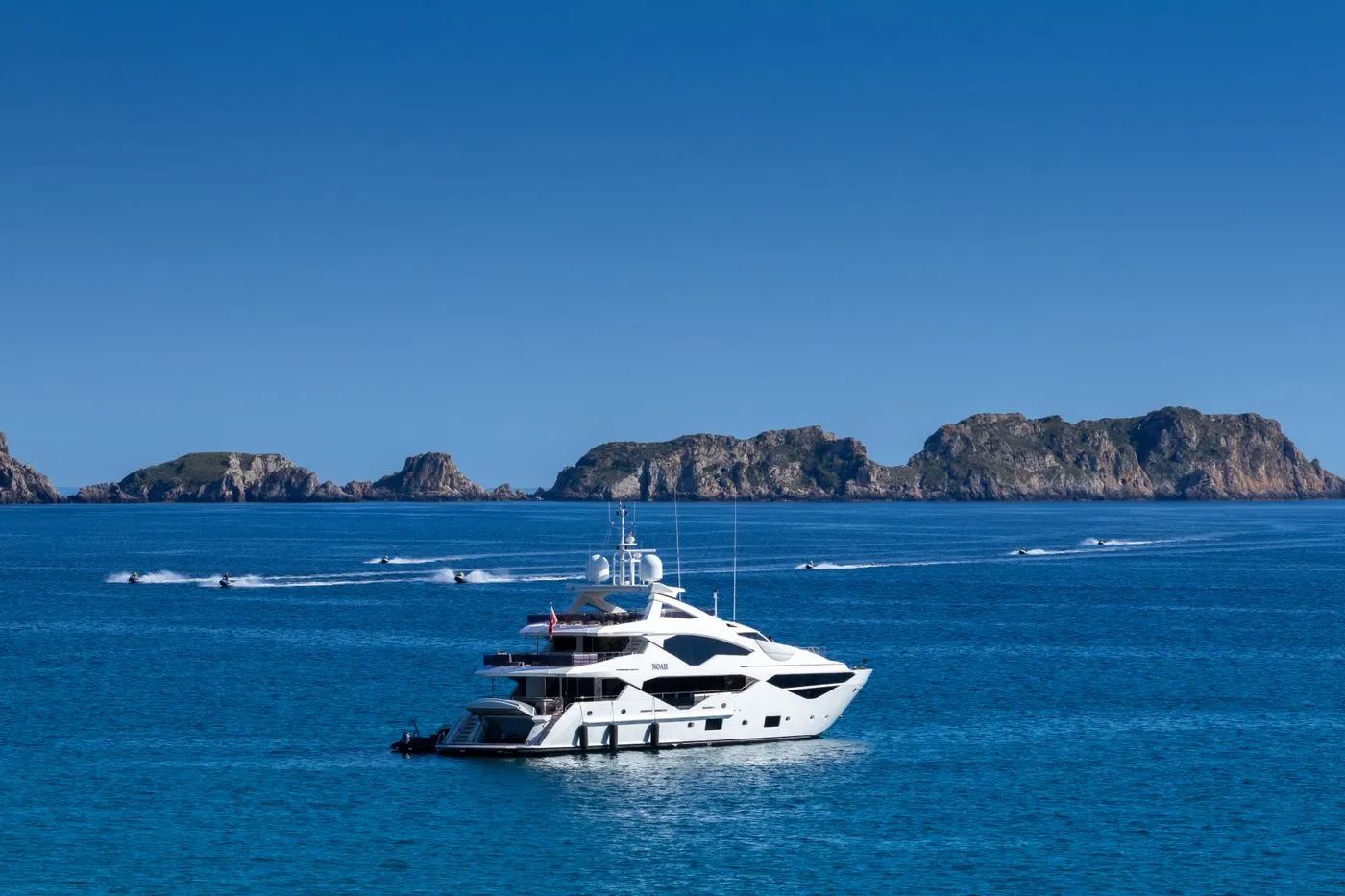 A superyacht at anchor on flat blue water with islands beyond