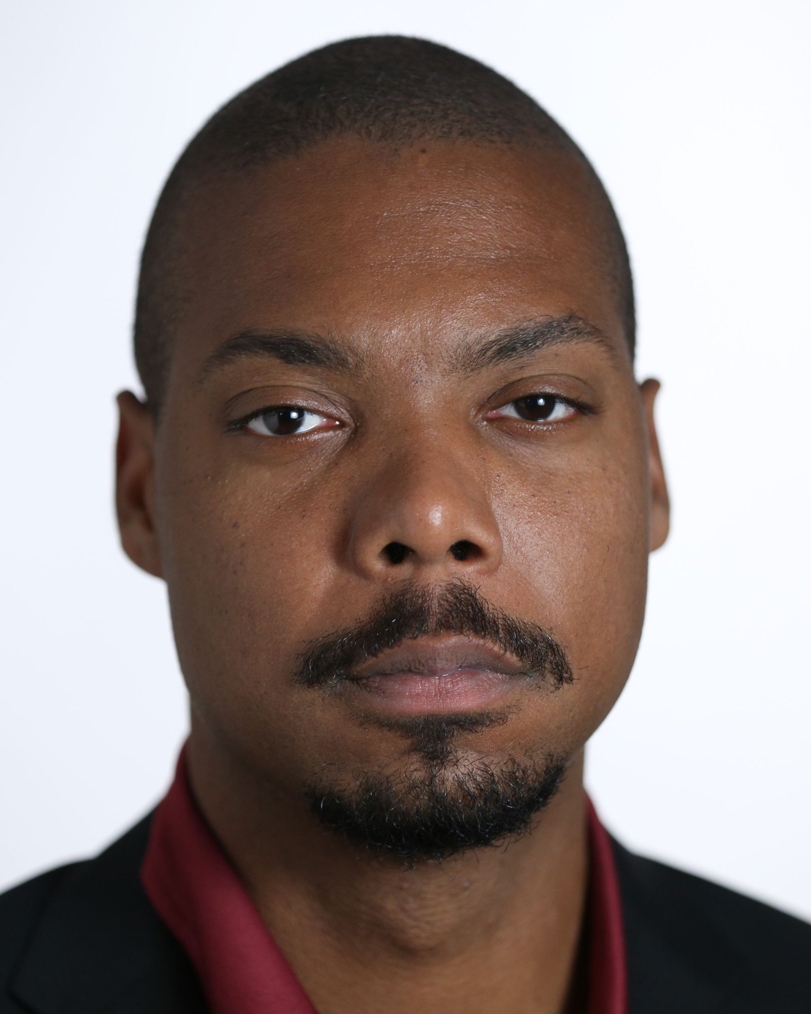 Portrait of a man in a dark jacket and burgundy shirt against a white background