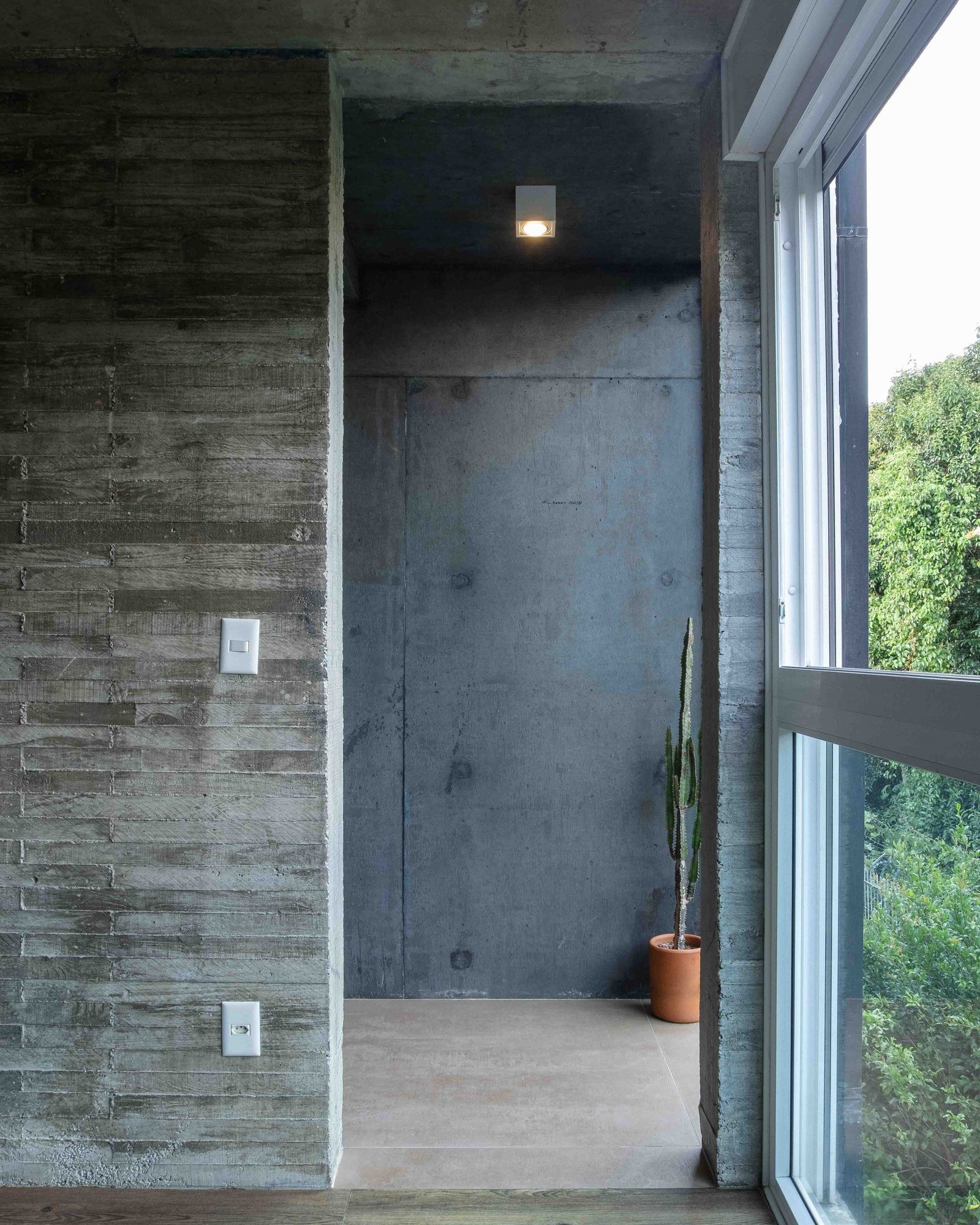 Board-marked concrete interior wall with a tall slot window onto trees