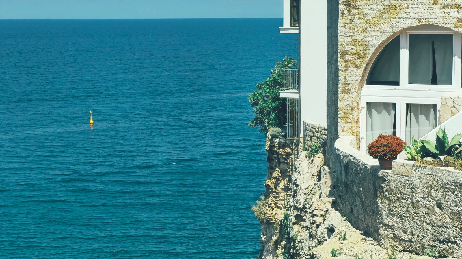 White house standing on a rocky headland above a deep blue sea