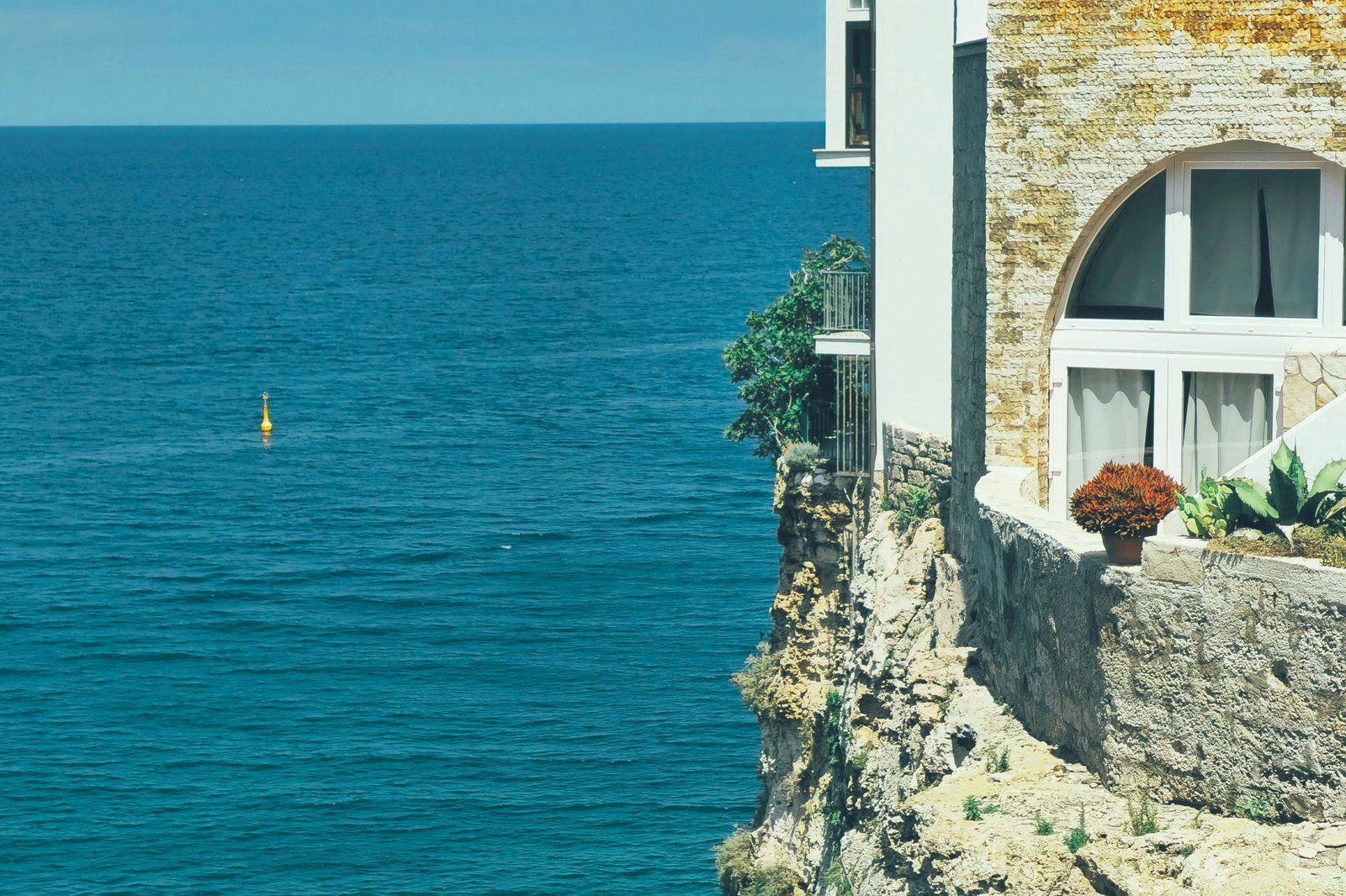 White house standing on a rocky headland above a deep blue sea