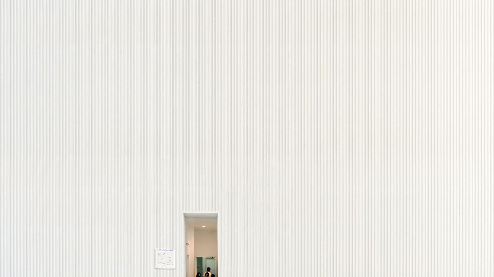 Large ribbed plaster wall with a small doorway and a figure passing through