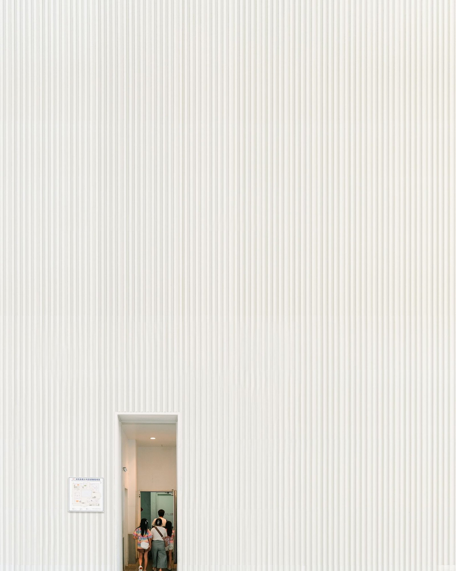 Large ribbed plaster wall with a small doorway and a figure passing through it