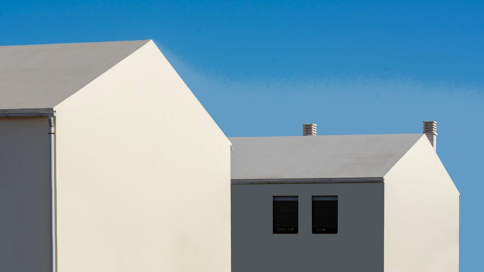 Cluster of white rendered volumes with pitched roofs against a clear blue sky