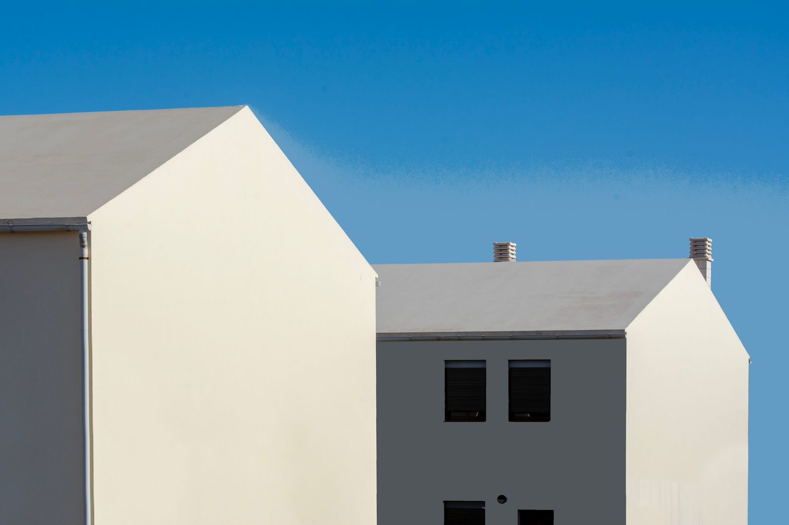 Cluster of white rendered volumes with pitched roofs against a clear blue sky