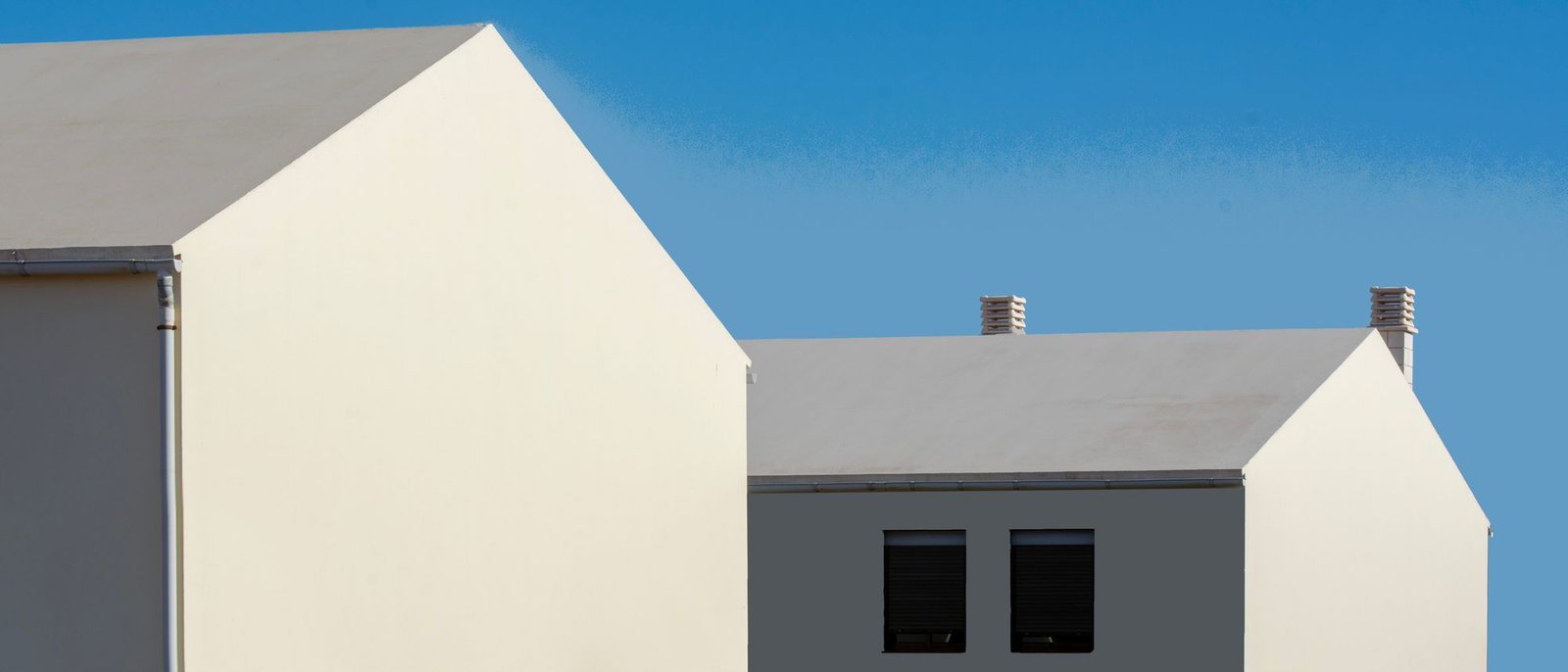 Cluster of white rendered volumes with pitched roofs against a clear blue sky