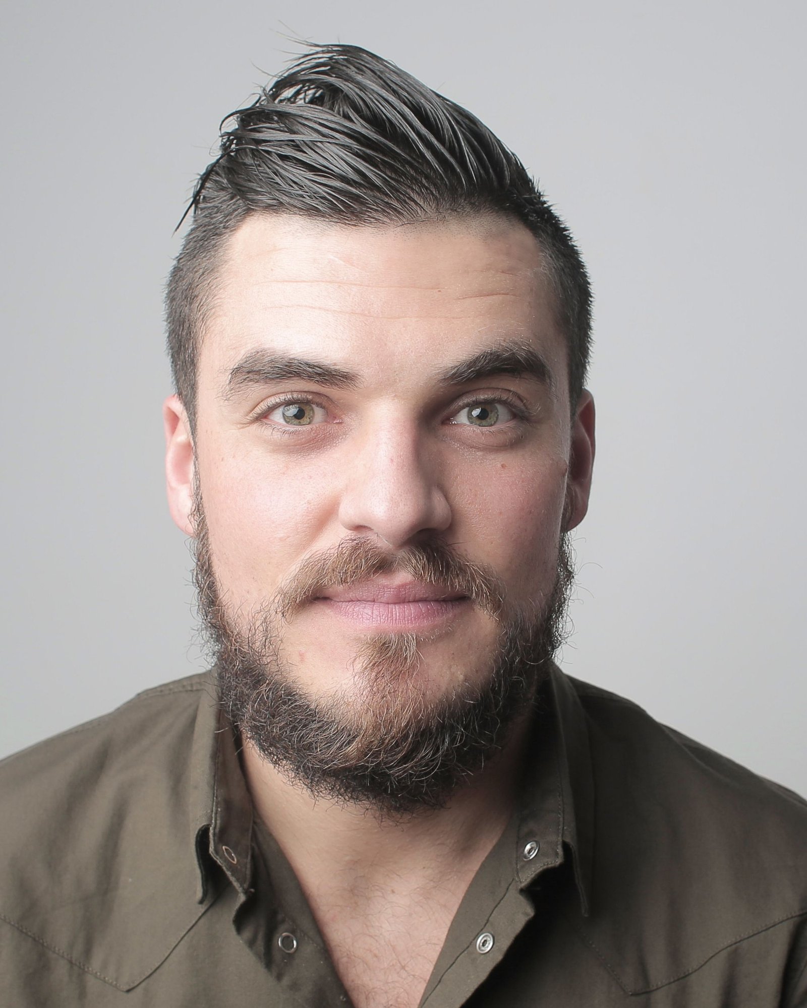 Portrait of a bearded man in a work jacket against a grey background