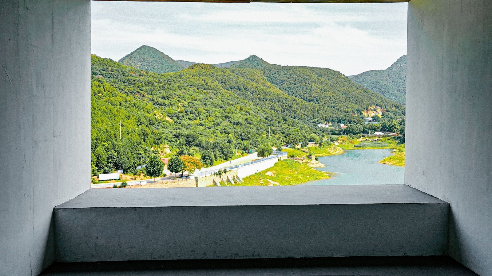 Concrete room with a full-width opening framing a river valley and mountains