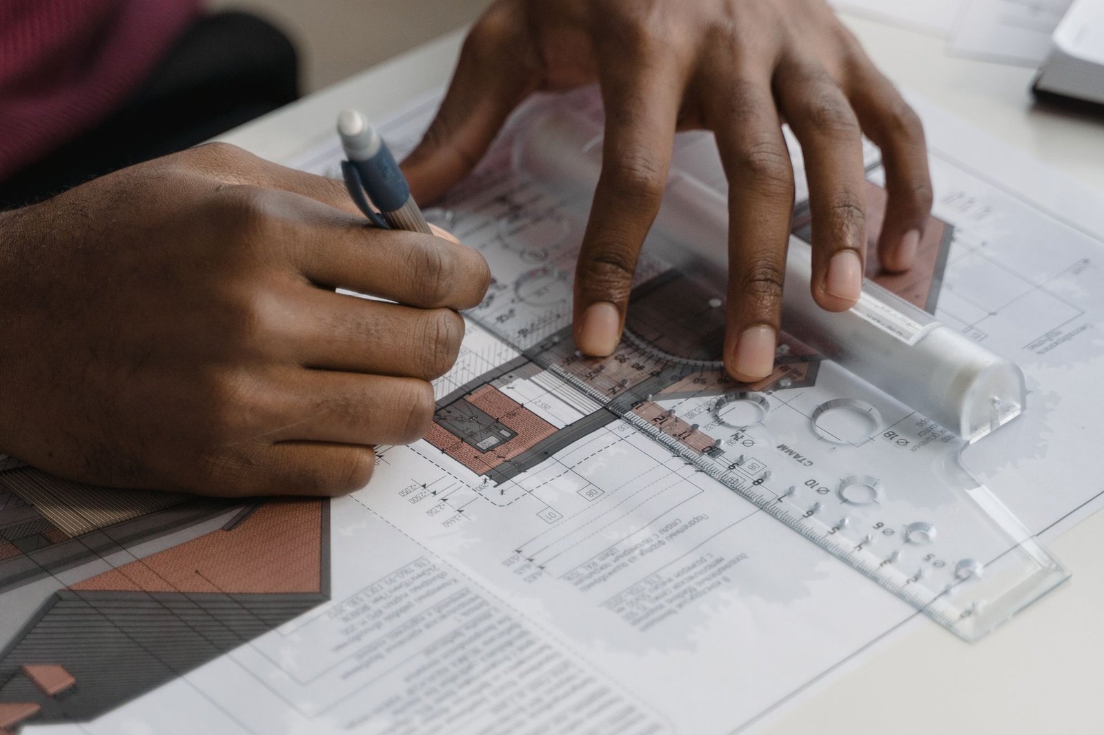 Hands working over a technical drawing with a scale rule and pencil