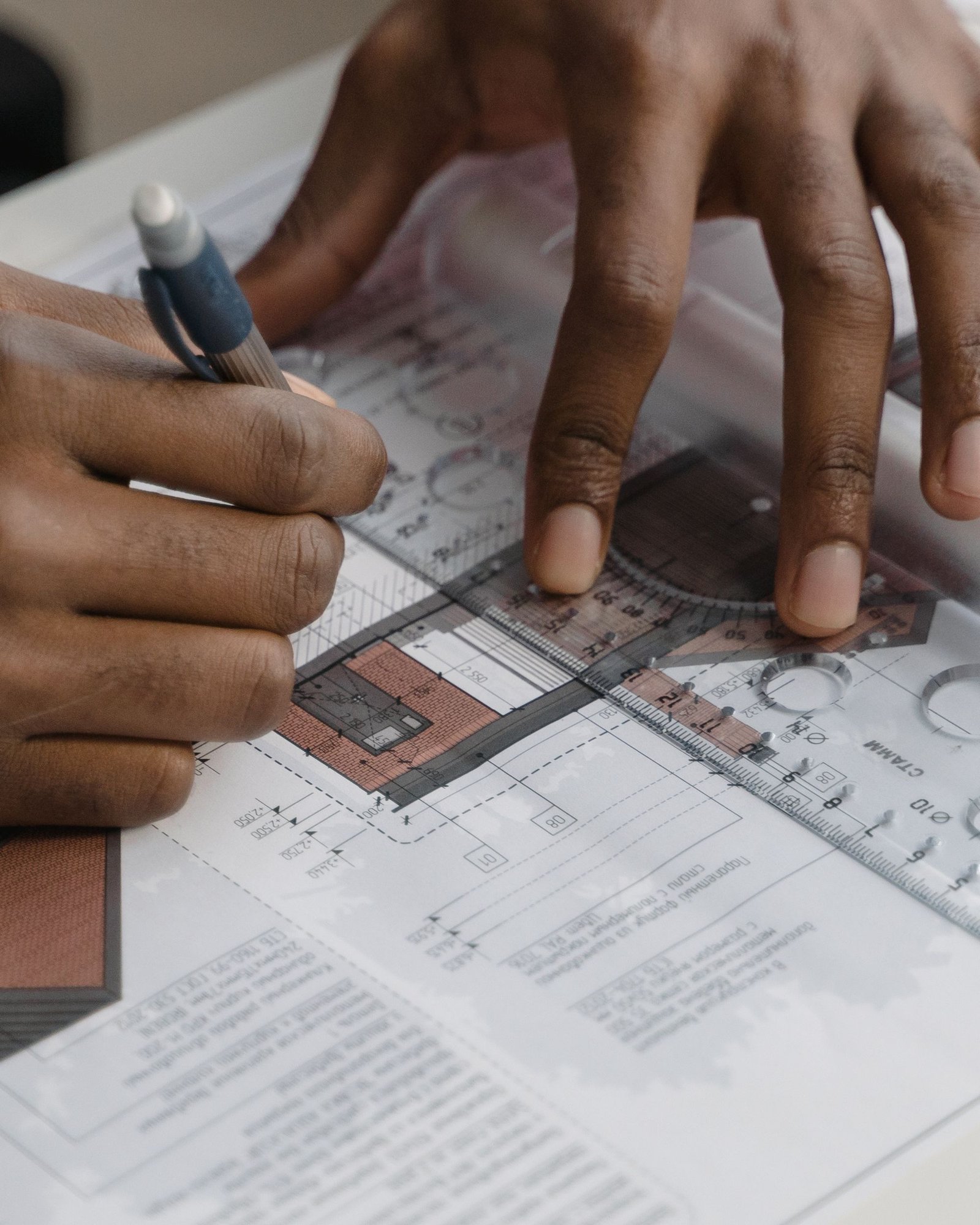 Hands working over a technical drawing with a scale rule and pencil