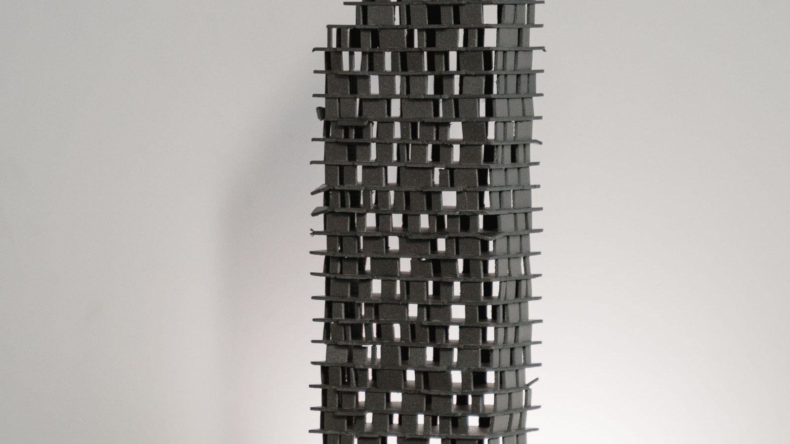 Dark perforated tower study model standing on a white plinth in a studio