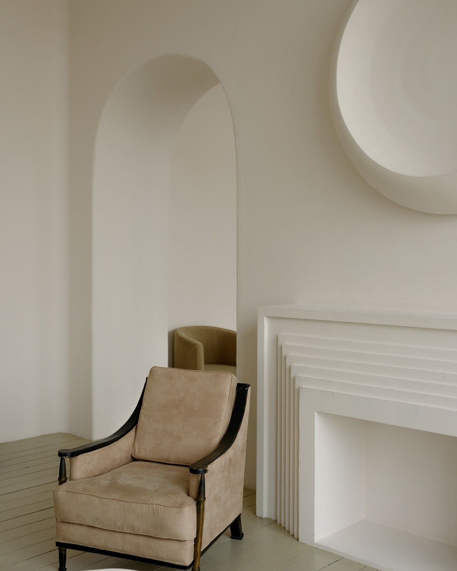 Pale room with an arched niche and a single upholstered chair