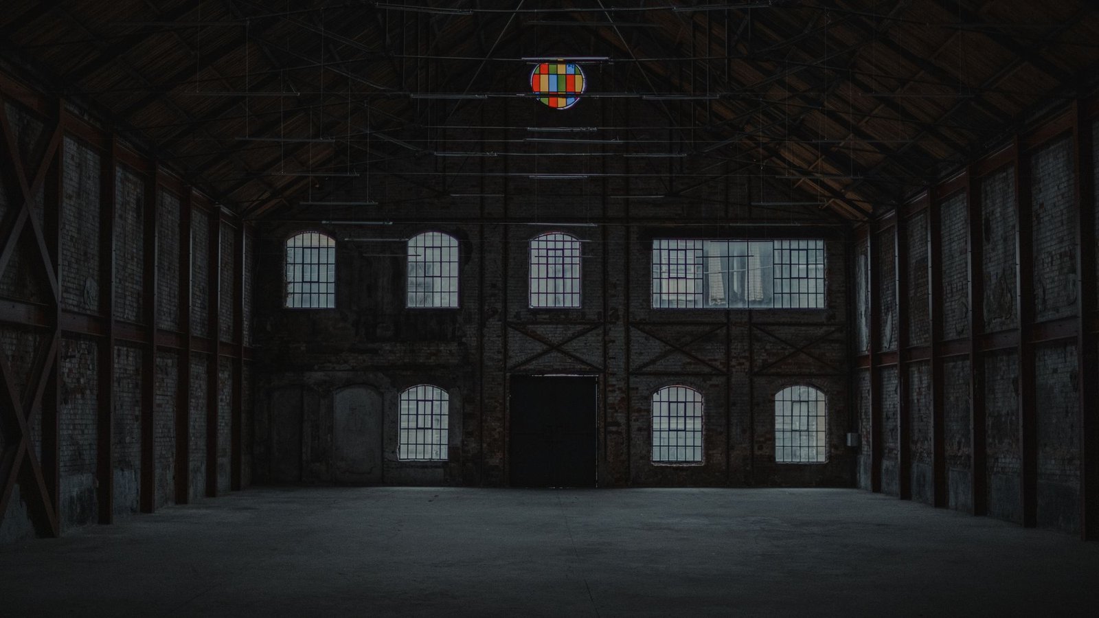 Vast empty industrial hall with tall arched windows and a bare concrete floor