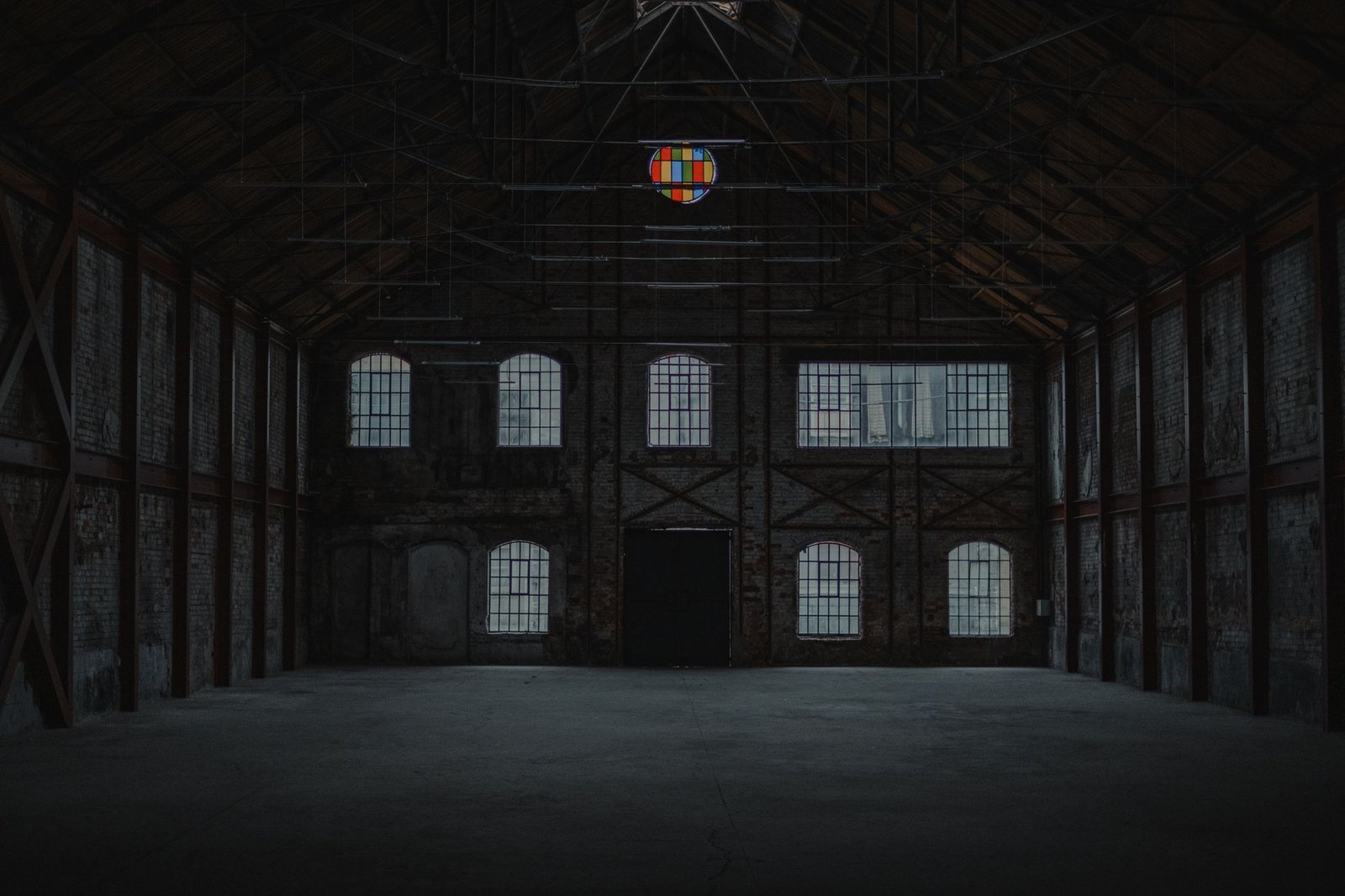 Vast empty industrial hall with tall arched windows and a bare concrete floor