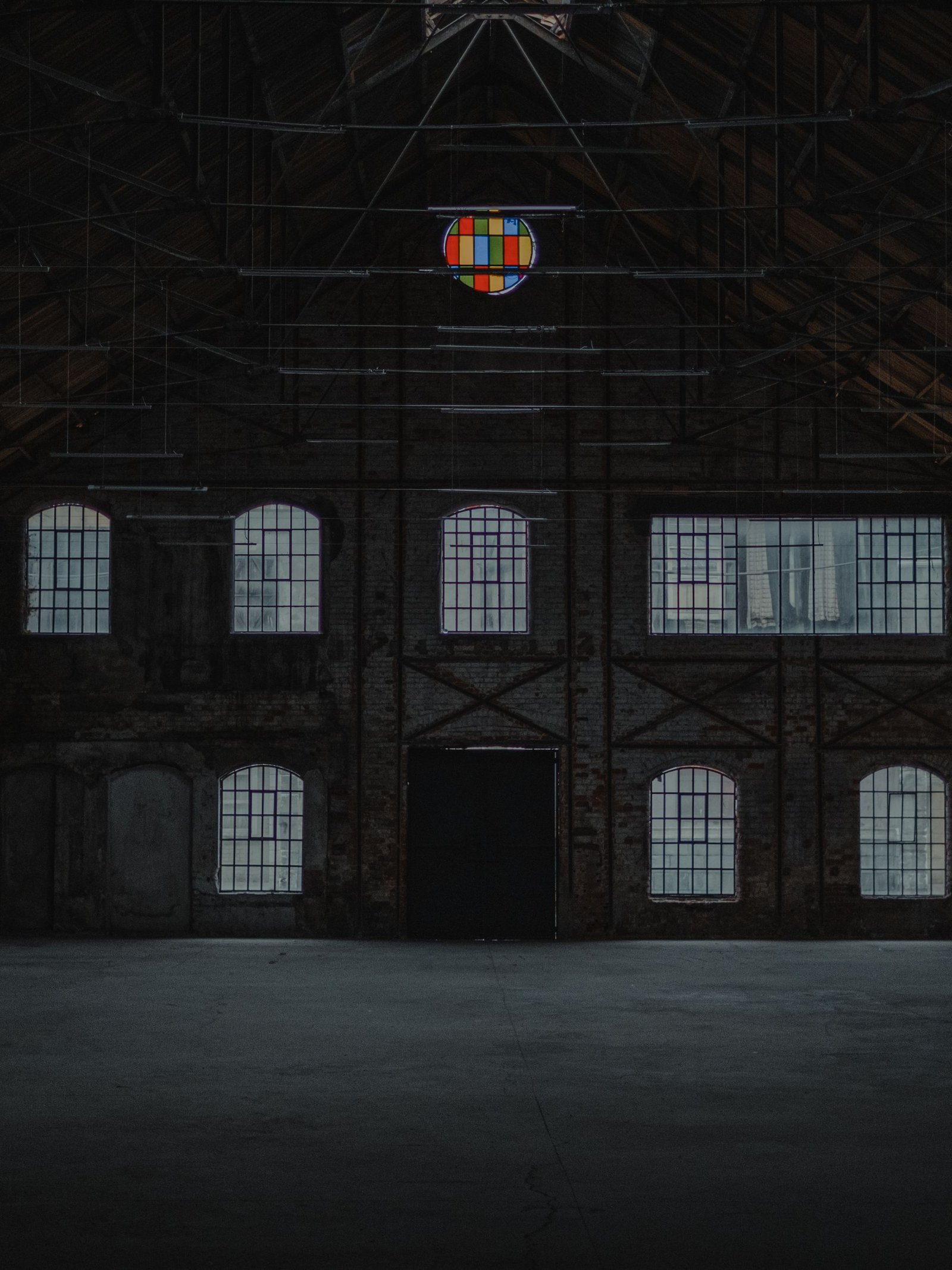 Vast empty industrial hall with tall arched windows and a bare concrete floor