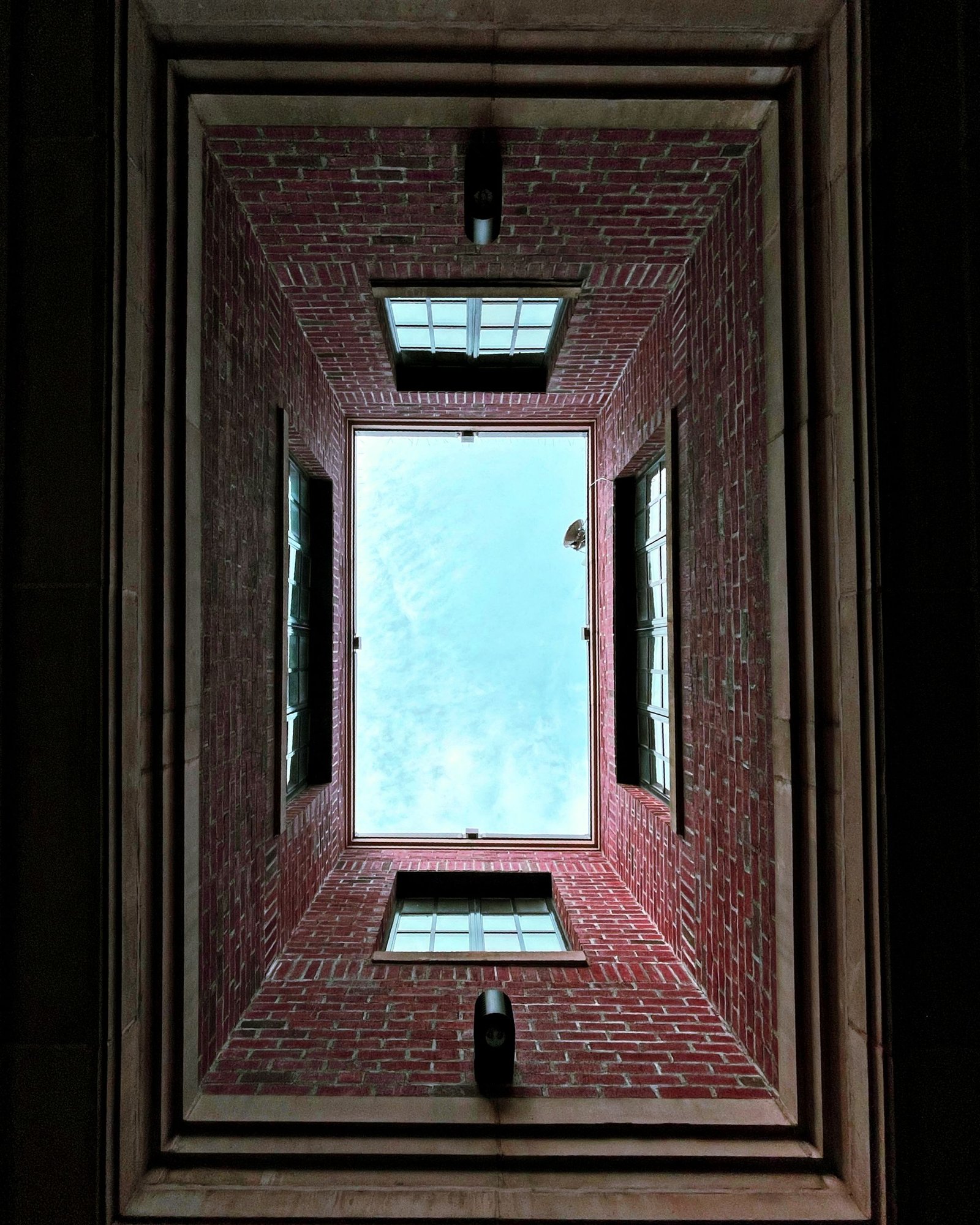 Looking up a narrow brick light shaft to a square of bright sky