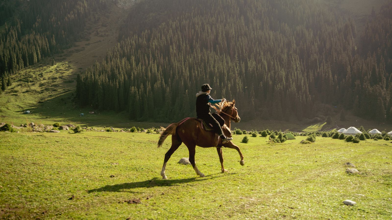 A rider on horseback crossing a green mountain valley