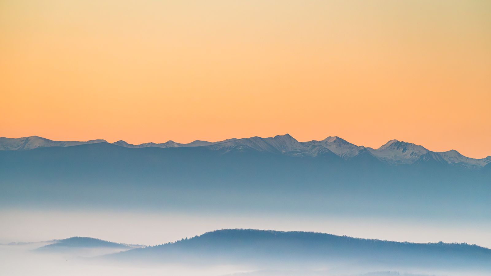 Pastel dawn light over layered misty mountain ridges